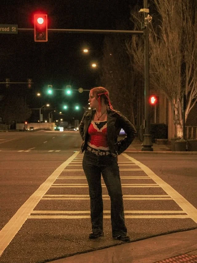 A woman stands on a crosswalk at night, looking down the street.