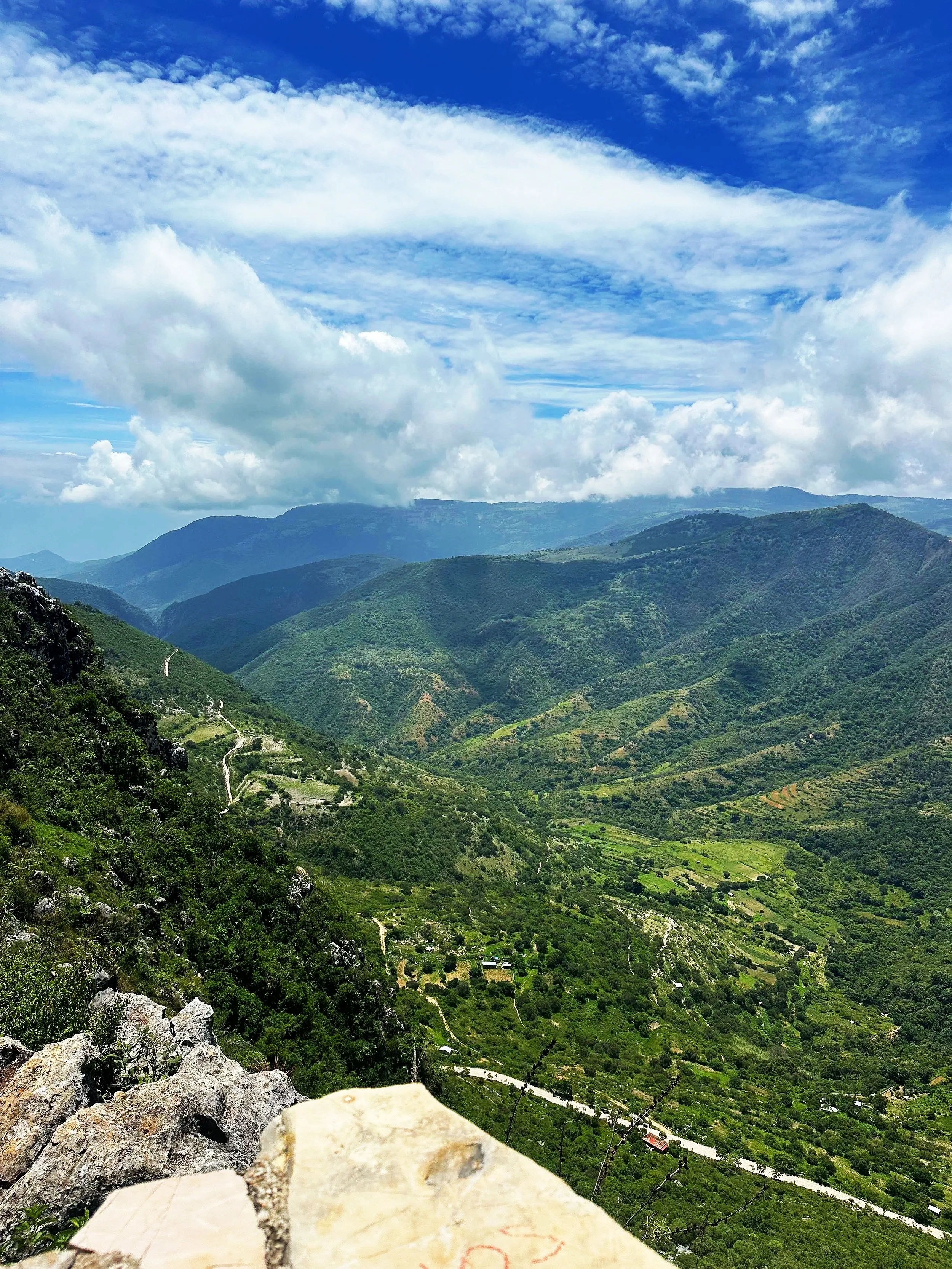 Scenic view of lush green mountains with a winding road, under a partly cloudy sky.