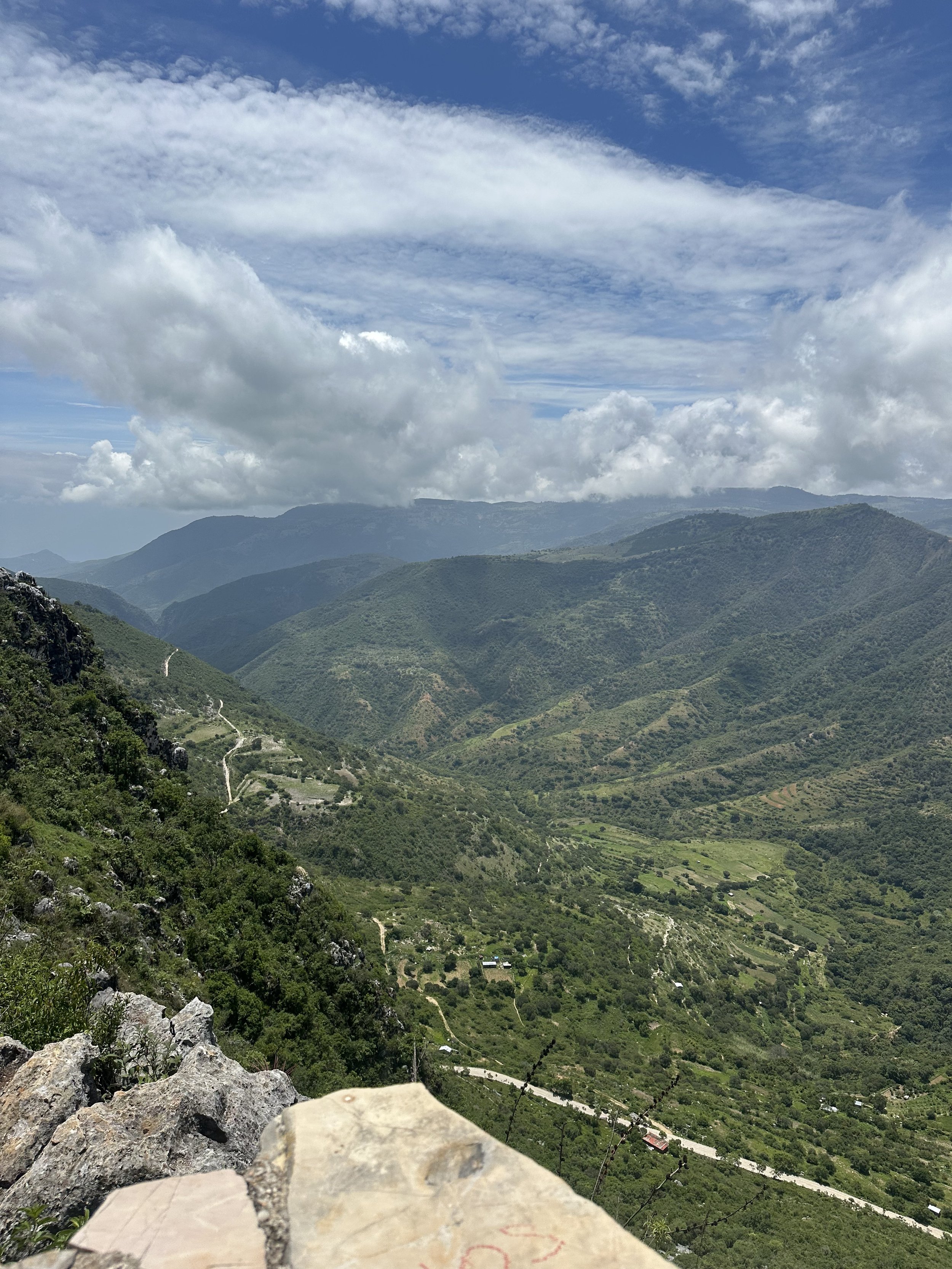 Scenic view of lush green mountains with a winding road, under a partly cloudy sky.