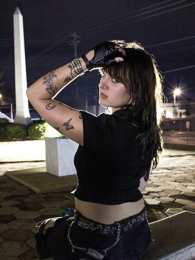 A woman sitting on a bench outside at night, silhouetted against a light, with a monument in the background.