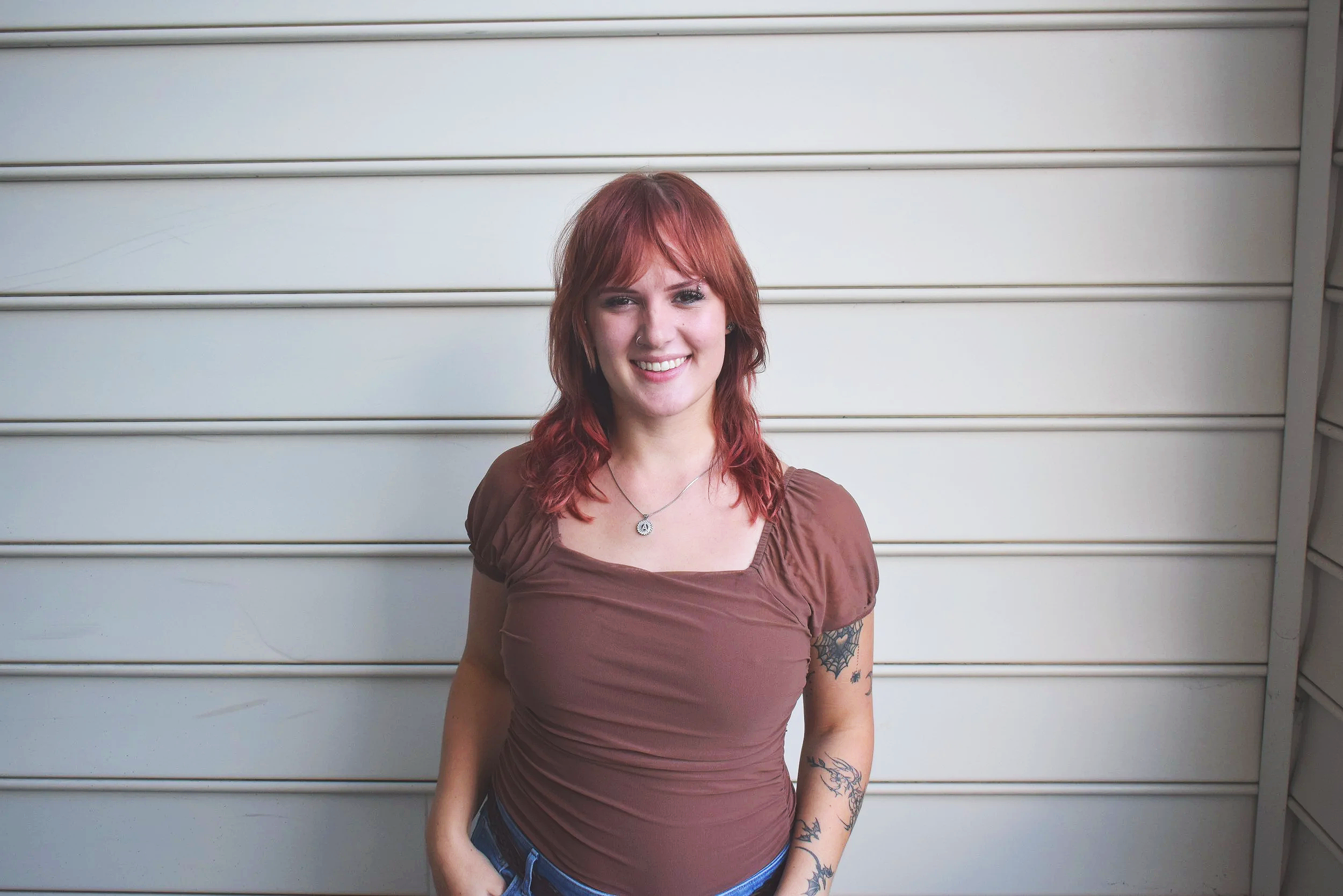 A young woman with red hair smiling and standing in front of a white metal garage door.