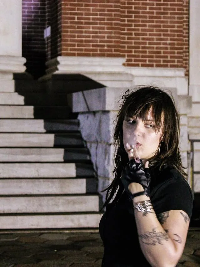 A woman smoking at night with stairs in the background.