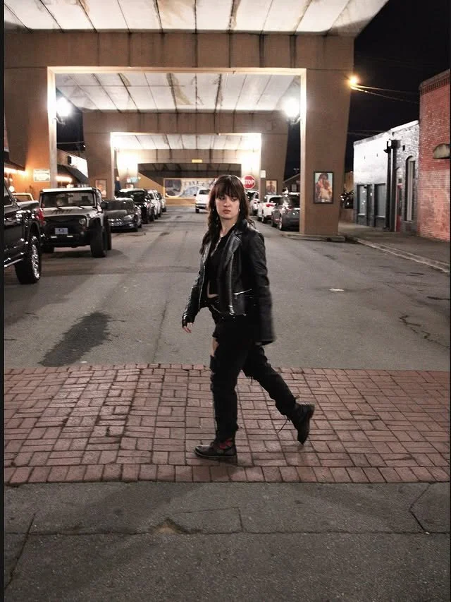 A woman crossing a street under a bridge at night.