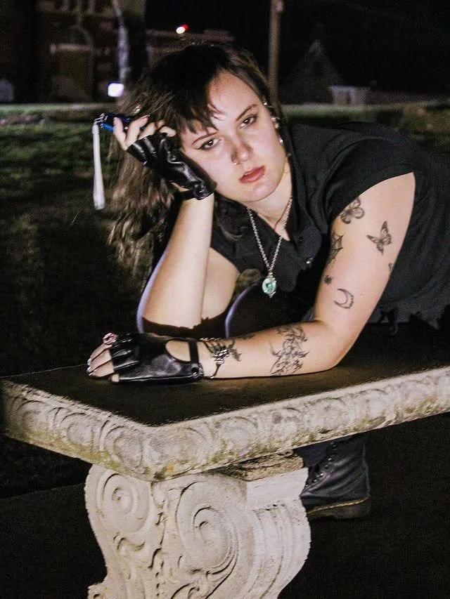 A woman lying on a bench outside at night.
