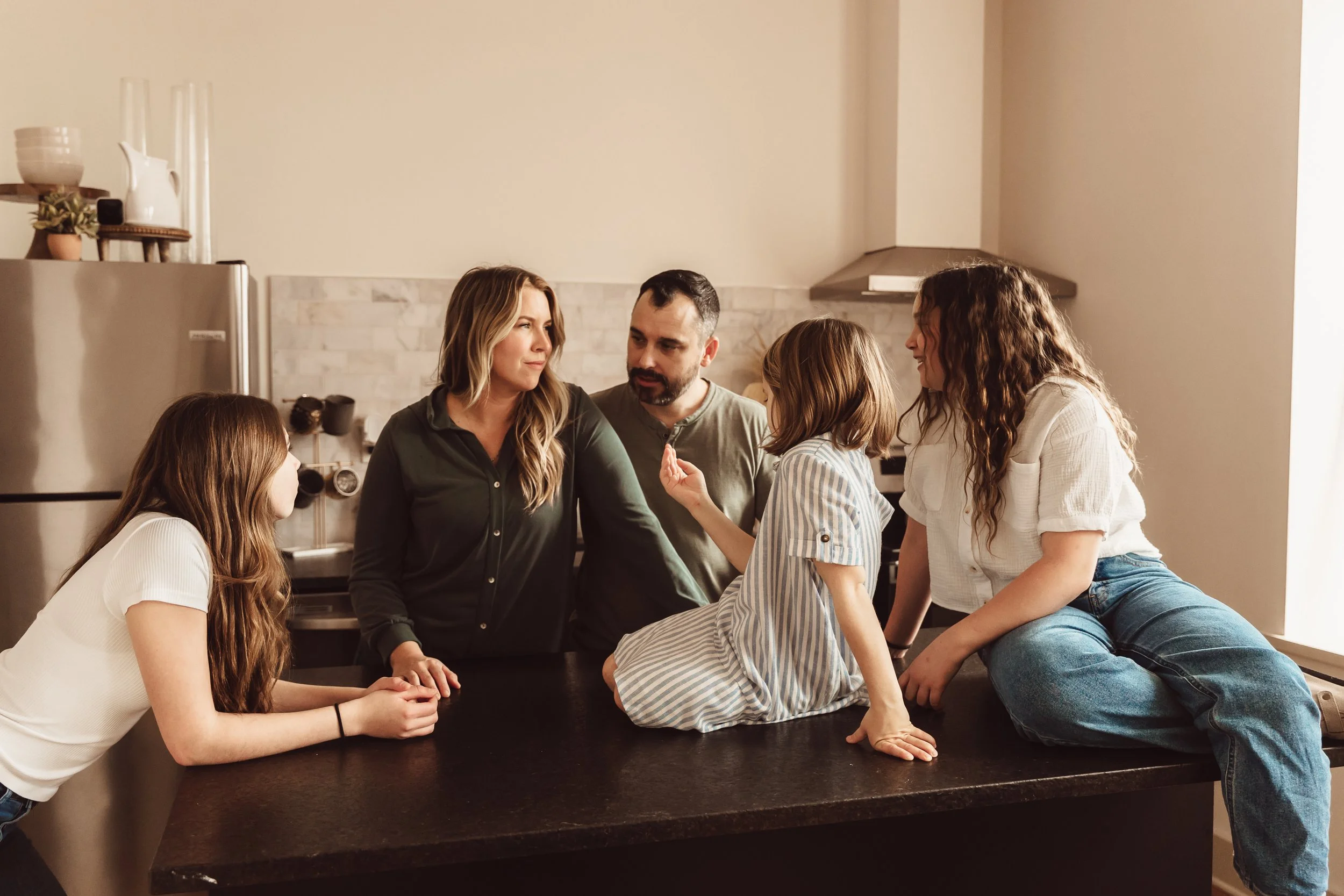 A family gathered around a kitchen island, having a serious conversation, with children and adults interacting.
