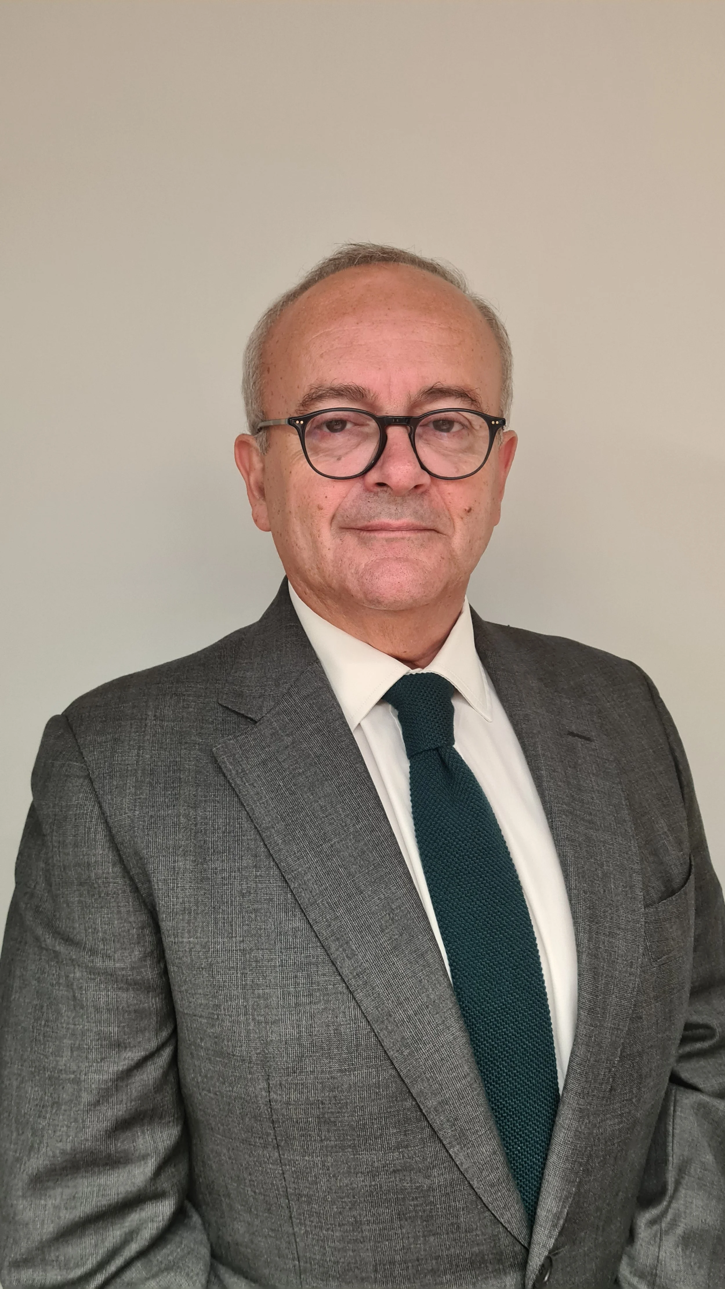 Man in a gray suit and glasses standing against a plain background.