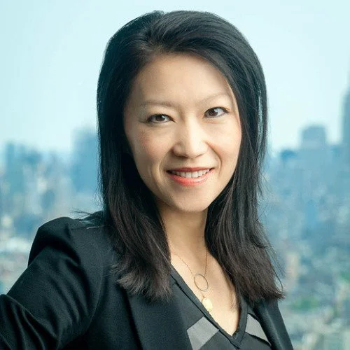 Smiling person with dark hair and pearl earrings in formal attire