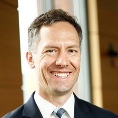 Smiling man in a suit with short hair, standing indoors.