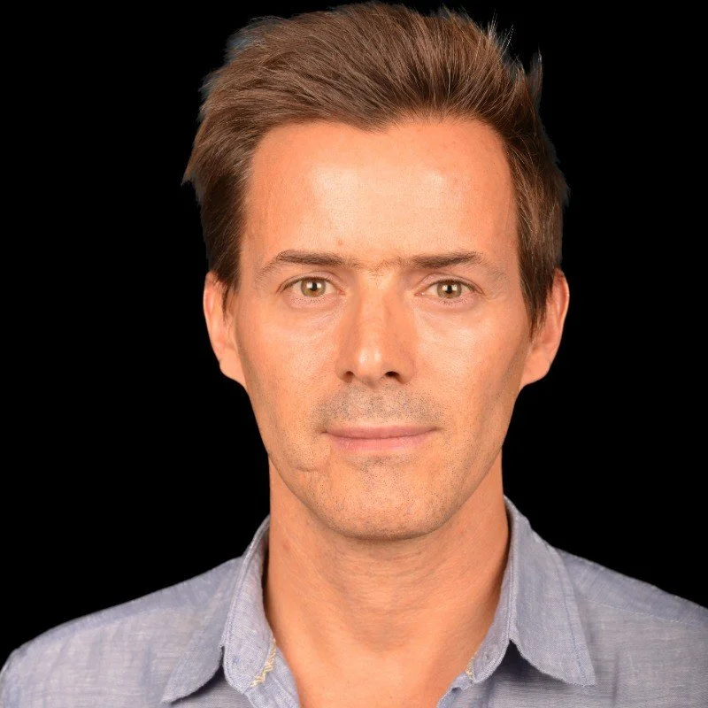 Portrait of a man with short hair wearing a blue button-up shirt against a dark background.