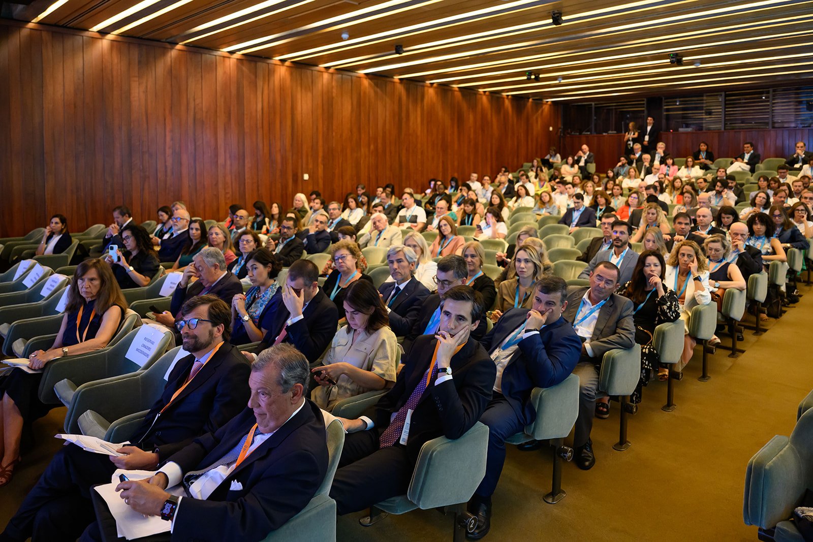 Conference attendees seated in a large auditorium, listening to a presentation.