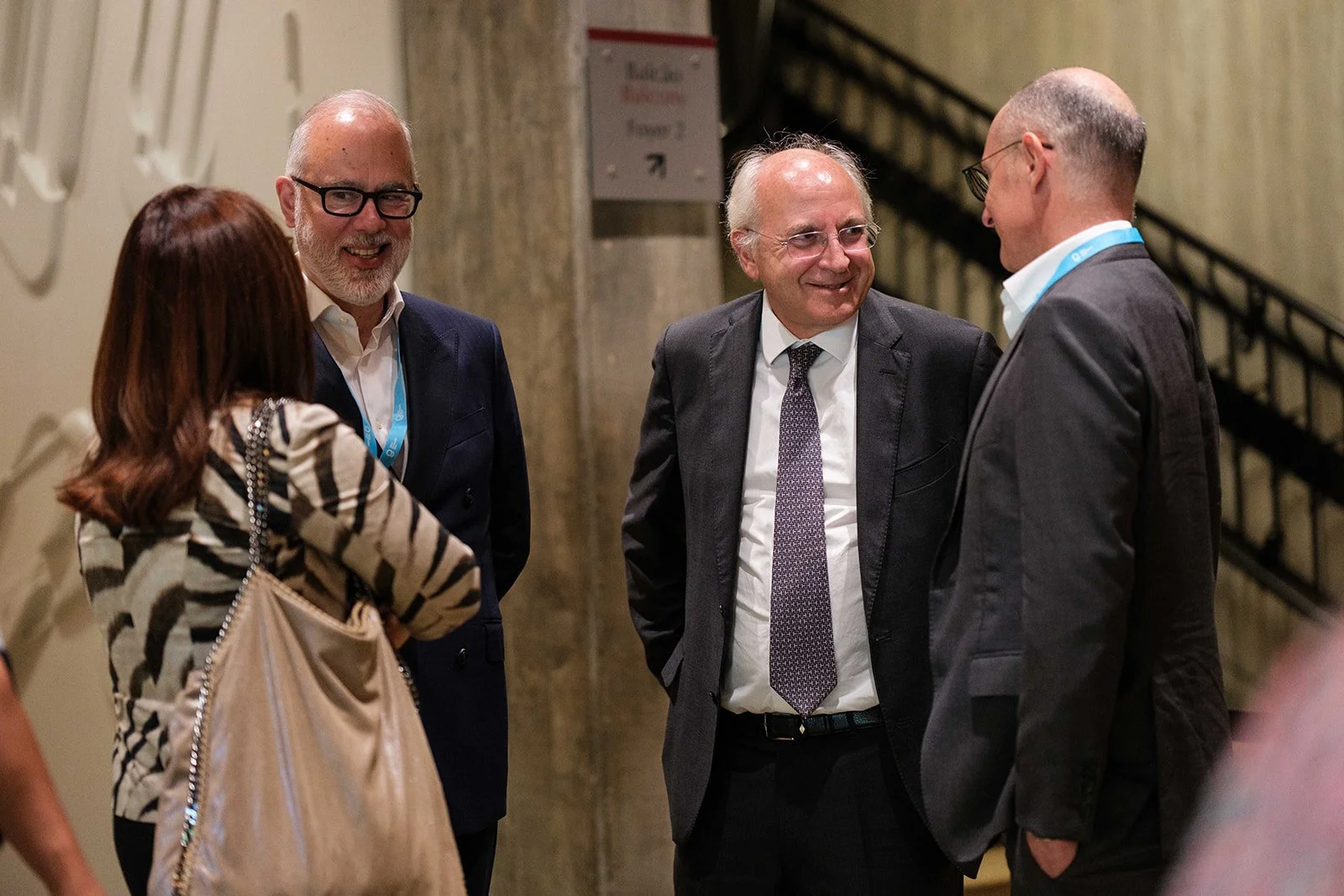 Four people, three men and one woman, are standing together and smiling during a conversation in an indoor setting.