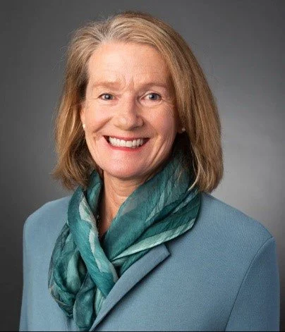 Smiling person wearing a blue blazer and green scarf