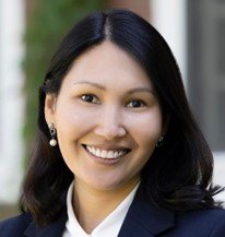 A woman with dark hair wearing earrings and a suit, smiling