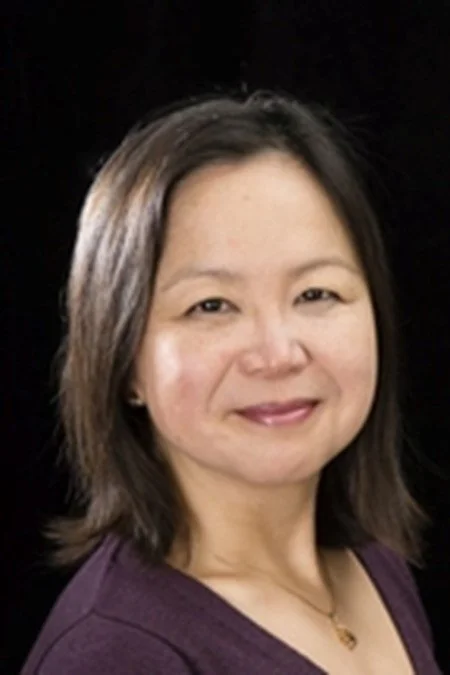 Portrait of a woman with shoulder-length hair against a black background, smiling gently.