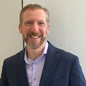 Smiling man in business suit standing against a light background.