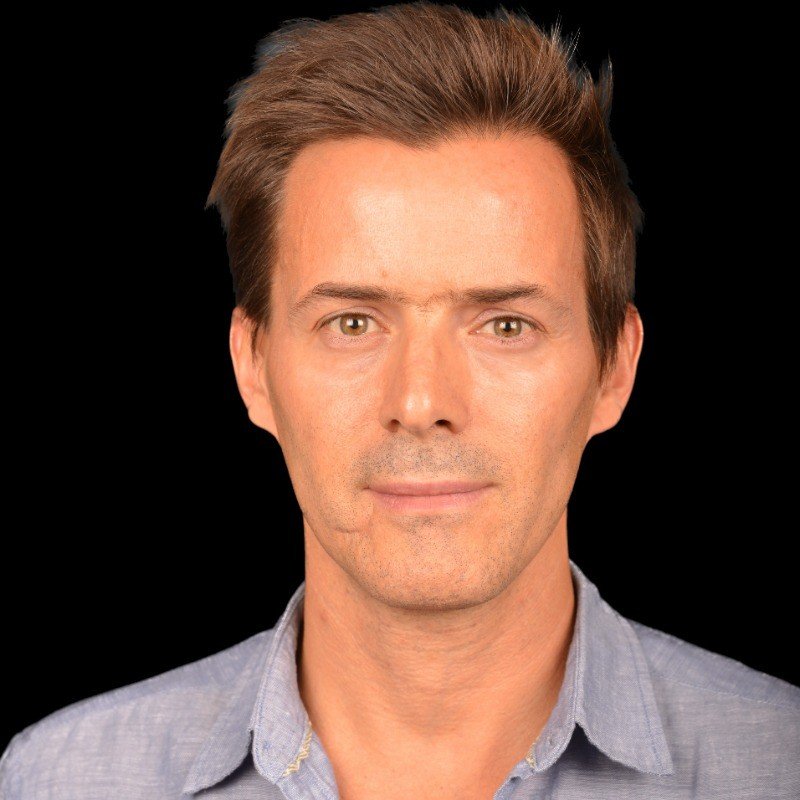 Portrait of a man with short brown hair, wearing a light blue button-up shirt, against a black background.