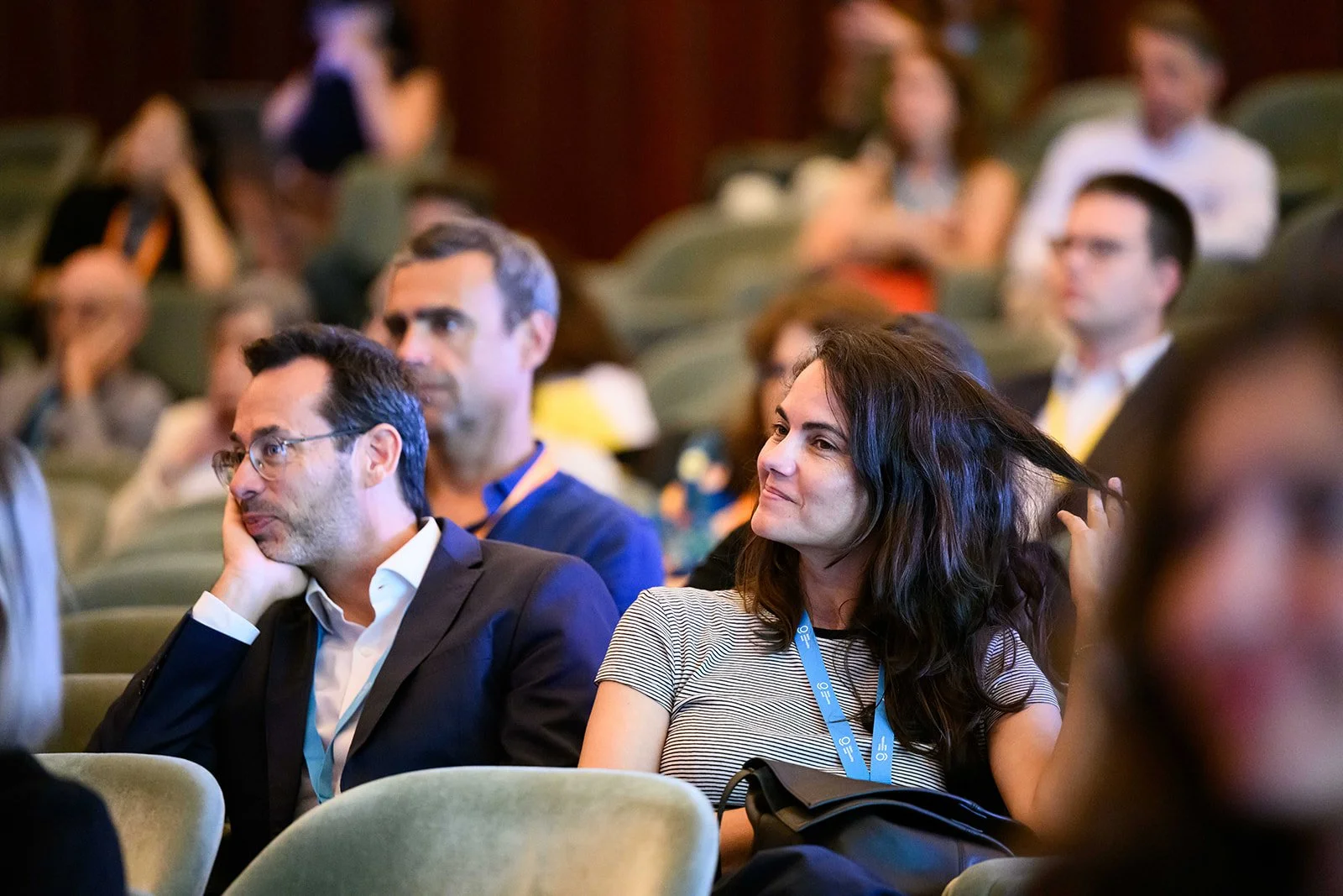 People attending a conference or seminar, seated in rows of chairs, listening attentively.