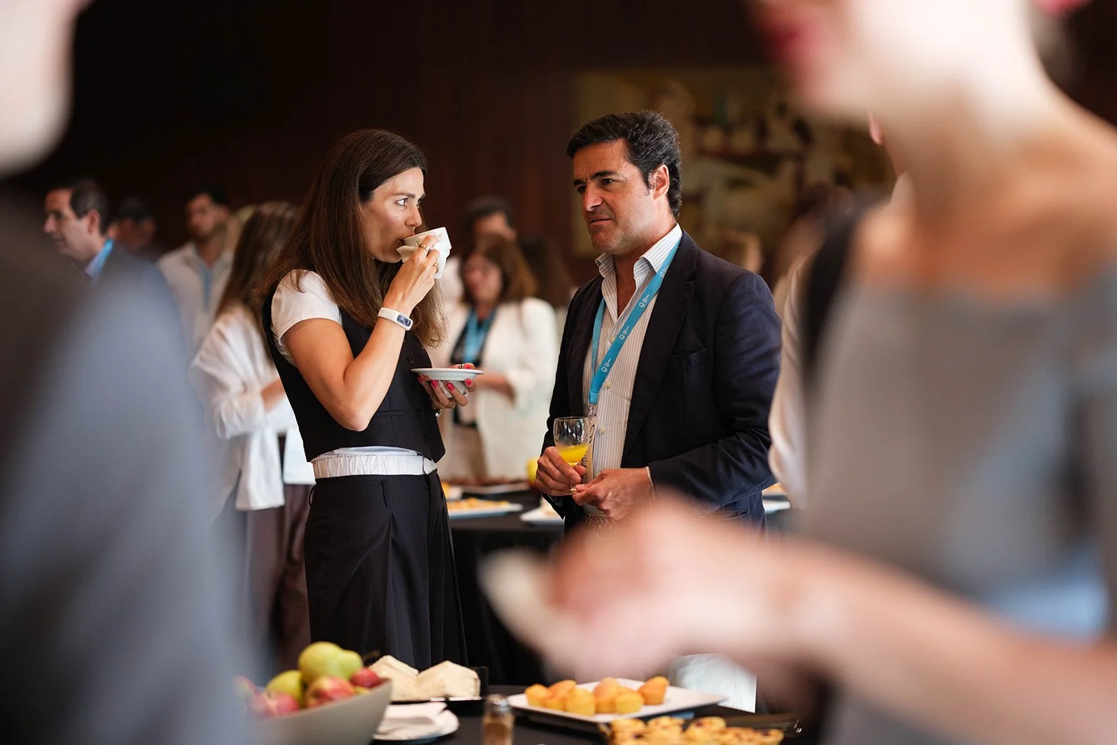 Two people having a conversation at a professional networking event, with a table of snacks and fruit in front of them.