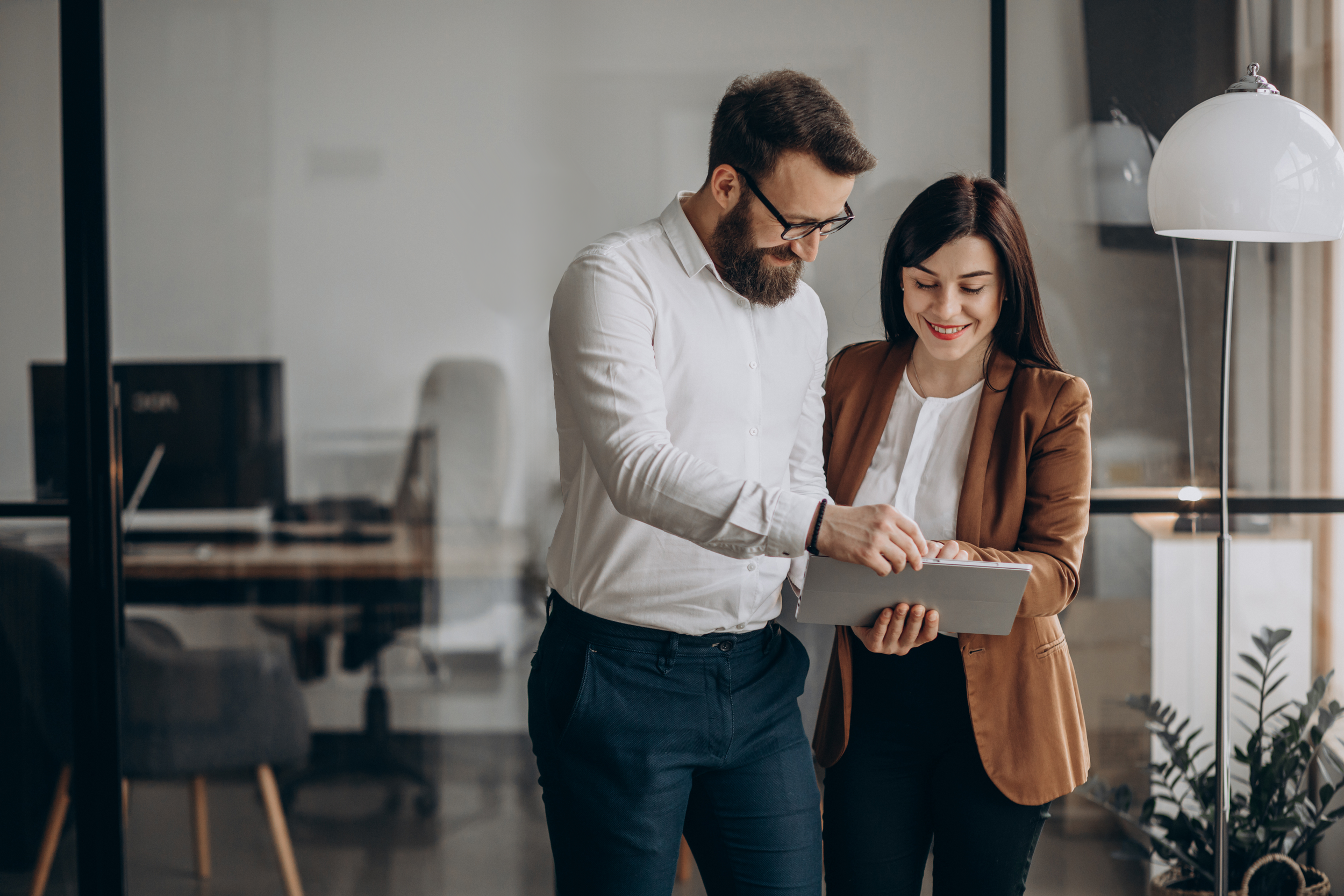 Two business professionals discussing over a tablet in a modern office setting.