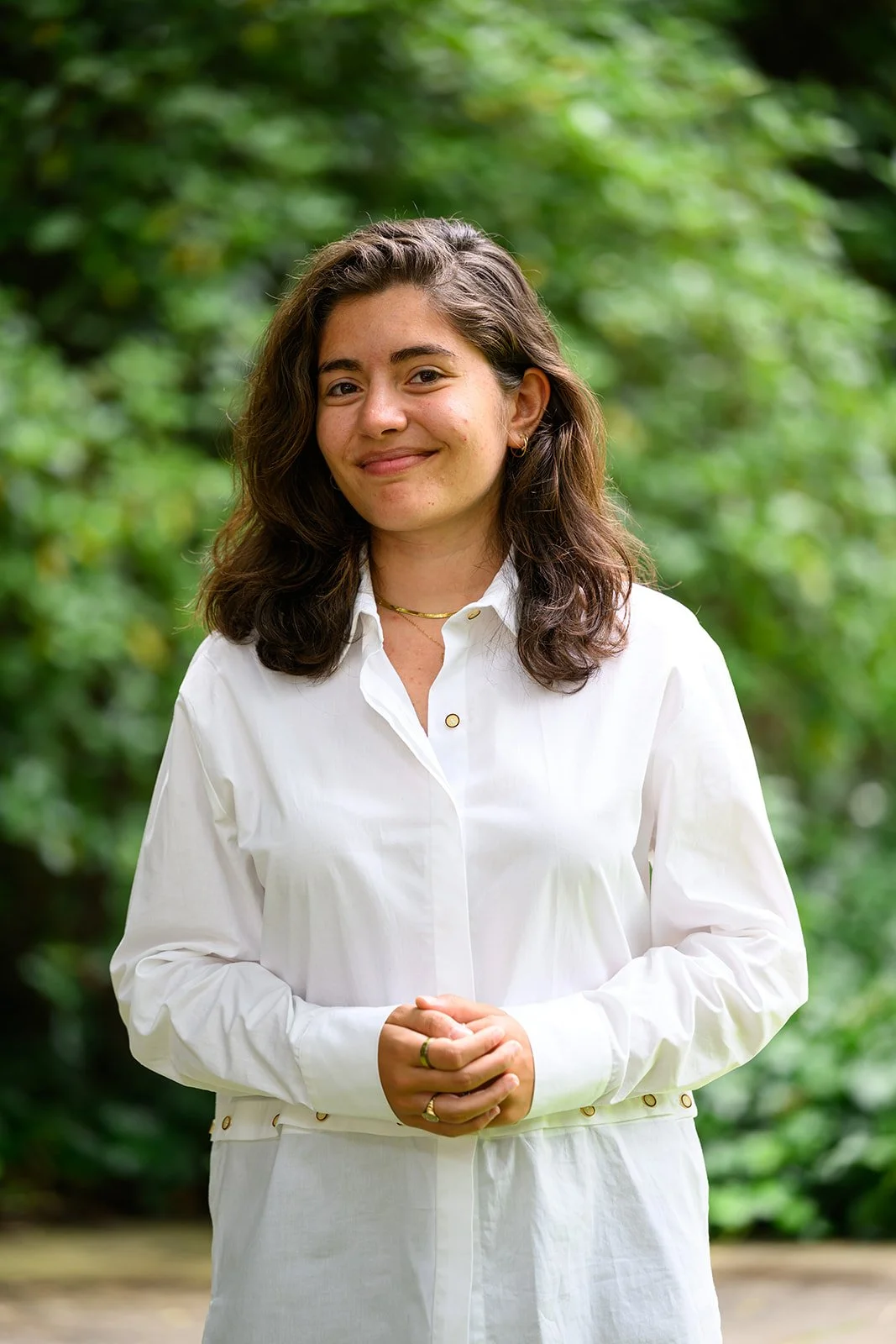 Woman in a beige blazer standing indoors near a modern atrium with greenery and glass walls.