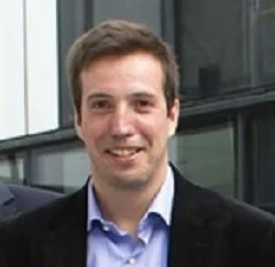 Portrait of a man in a blazer with a city building background.