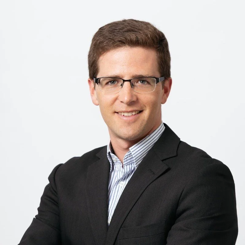 A man wearing glasses and a suit with a white background.