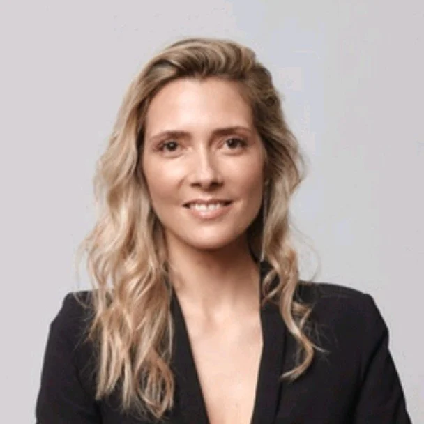 Woman with long blonde hair wearing a black blazer, smiling against a plain background.