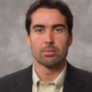 Portrait of a man in a suit with a gray background.