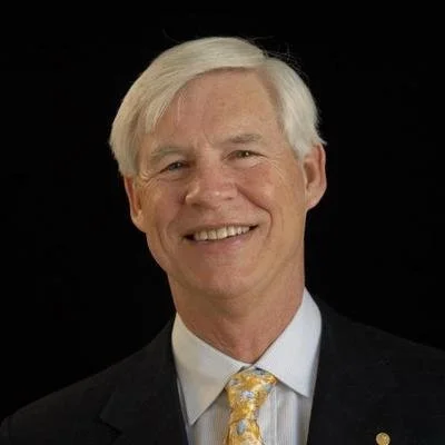 Smiling man in suit with light-colored hair and tie against black background
