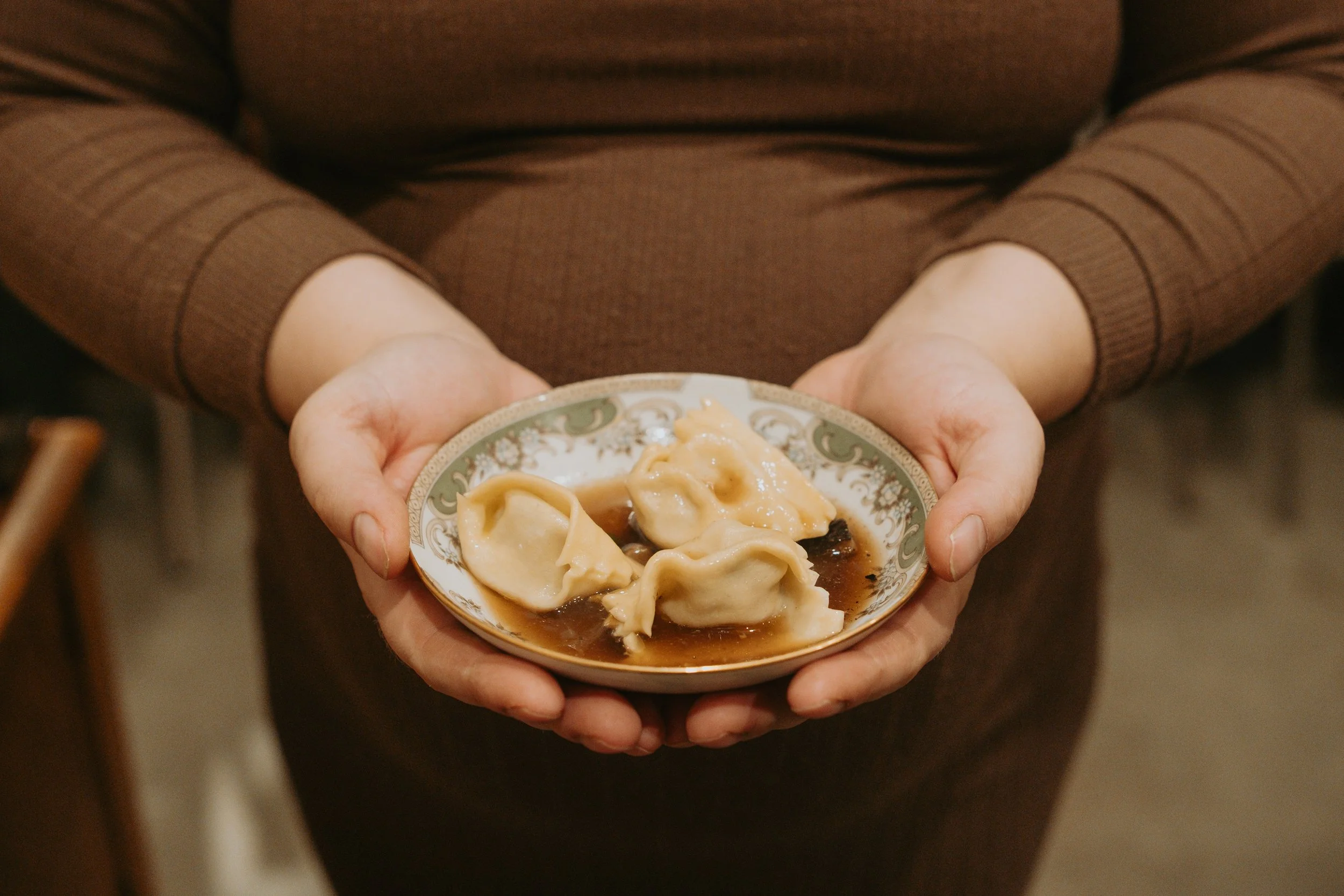 Une personne tient un plat de raviolis dans une main, avec une sauce sombre.
