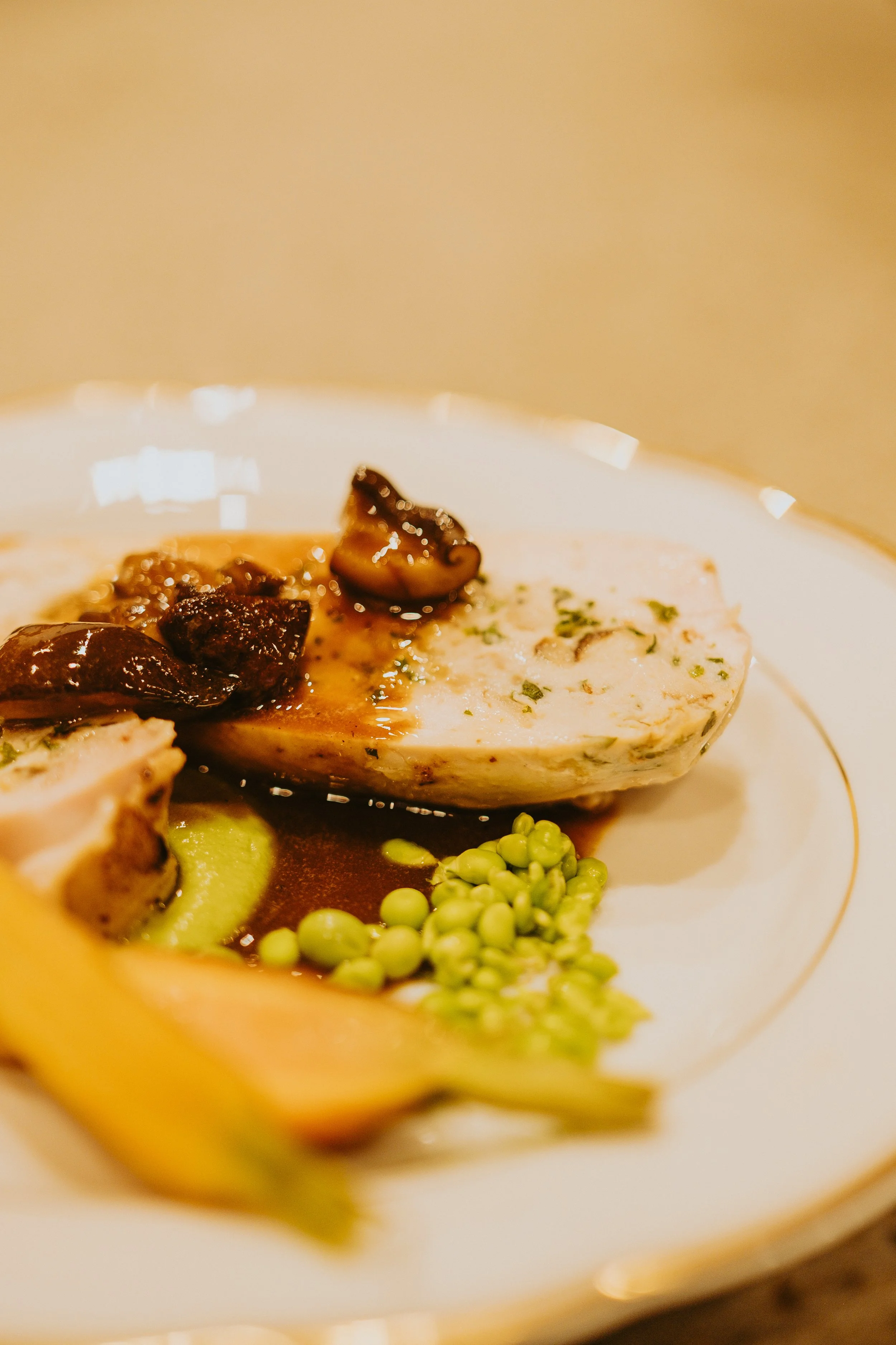 Assiette avec une portion de terrine garnie de champignons, accompagnée de légumes verts et de légumes jaunes, dans une sauce sombre.
