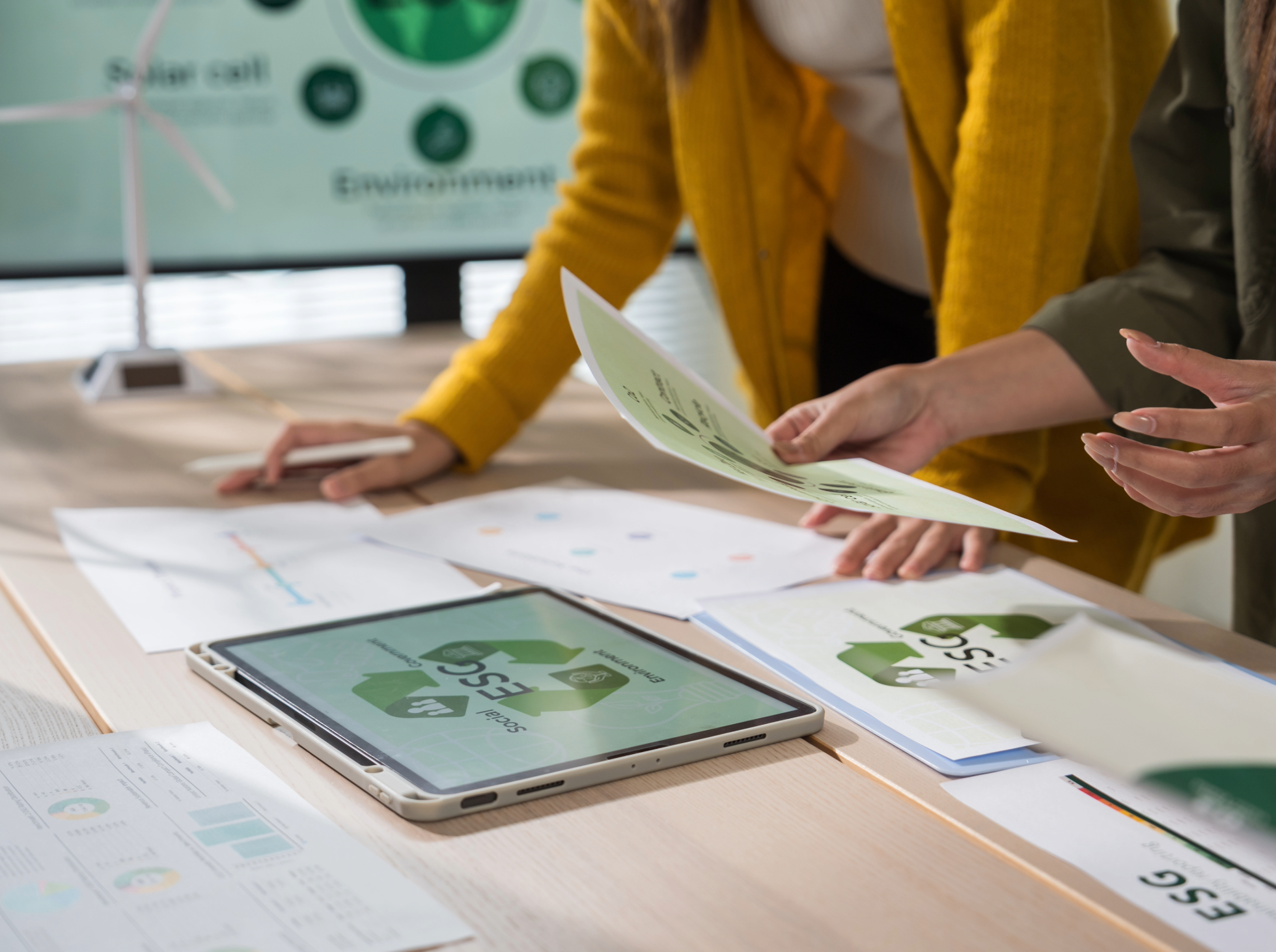 People engaged in a discussion about recycling, with documents and electronic devices on a table.