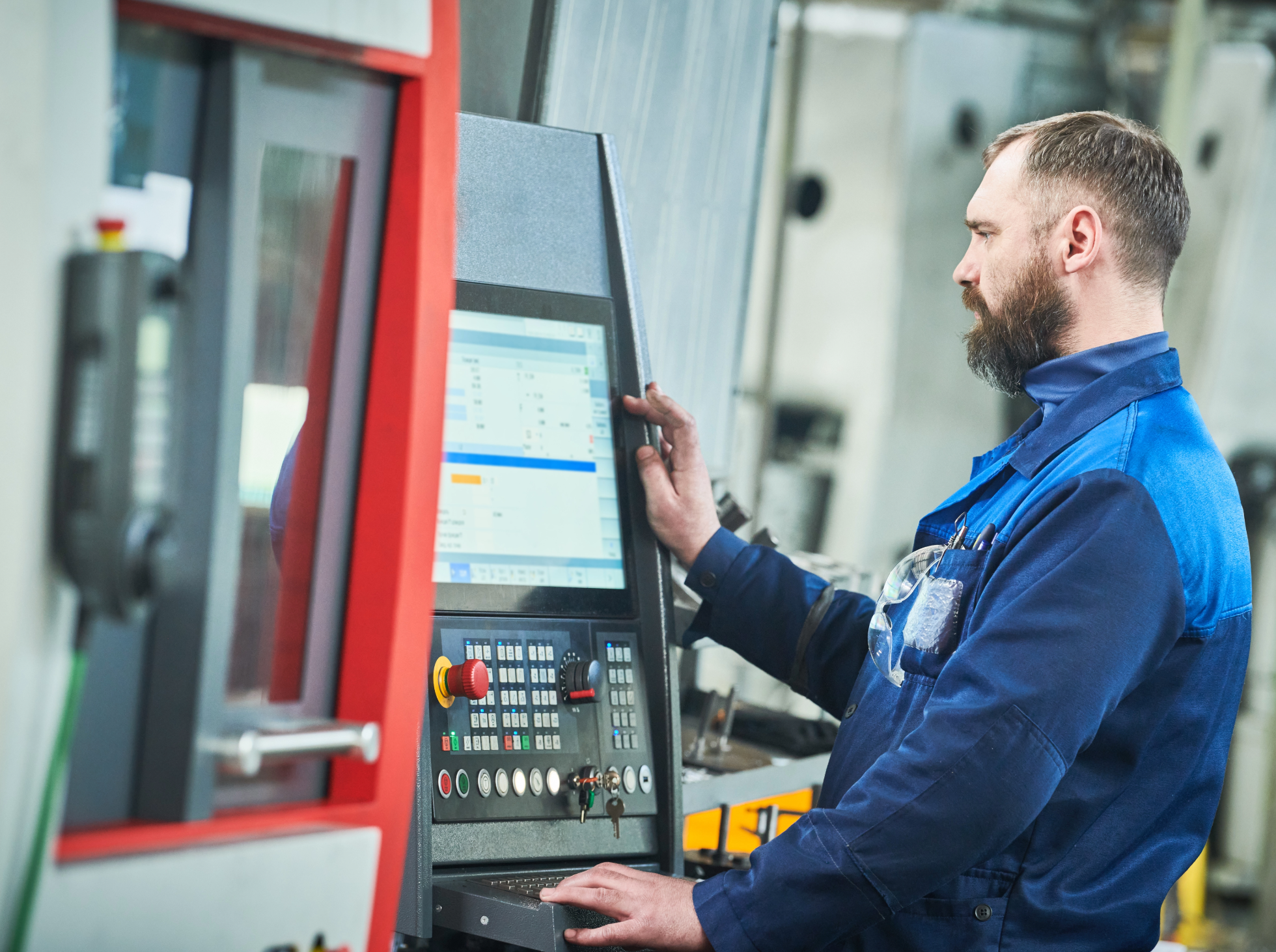 A man in blue work overalls operating CNC industrial machinery.