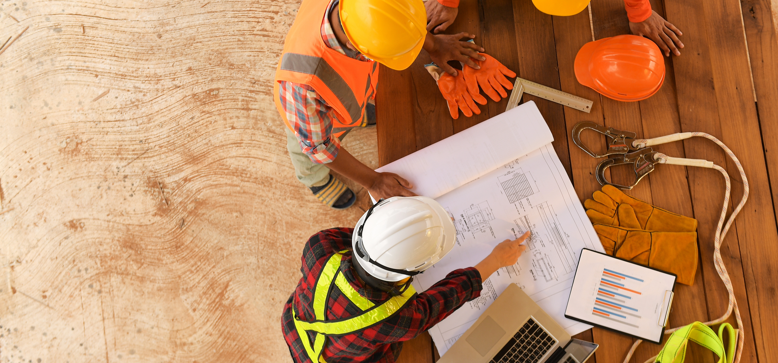 Construction engineers in safety gear studying blueprints at a construction site.