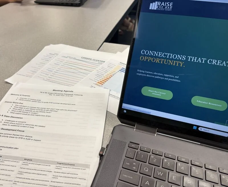 Laptop displaying a website with a blue and green theme, titled 'Connections That Create Opportunity,' alongside printed documents on a desk.