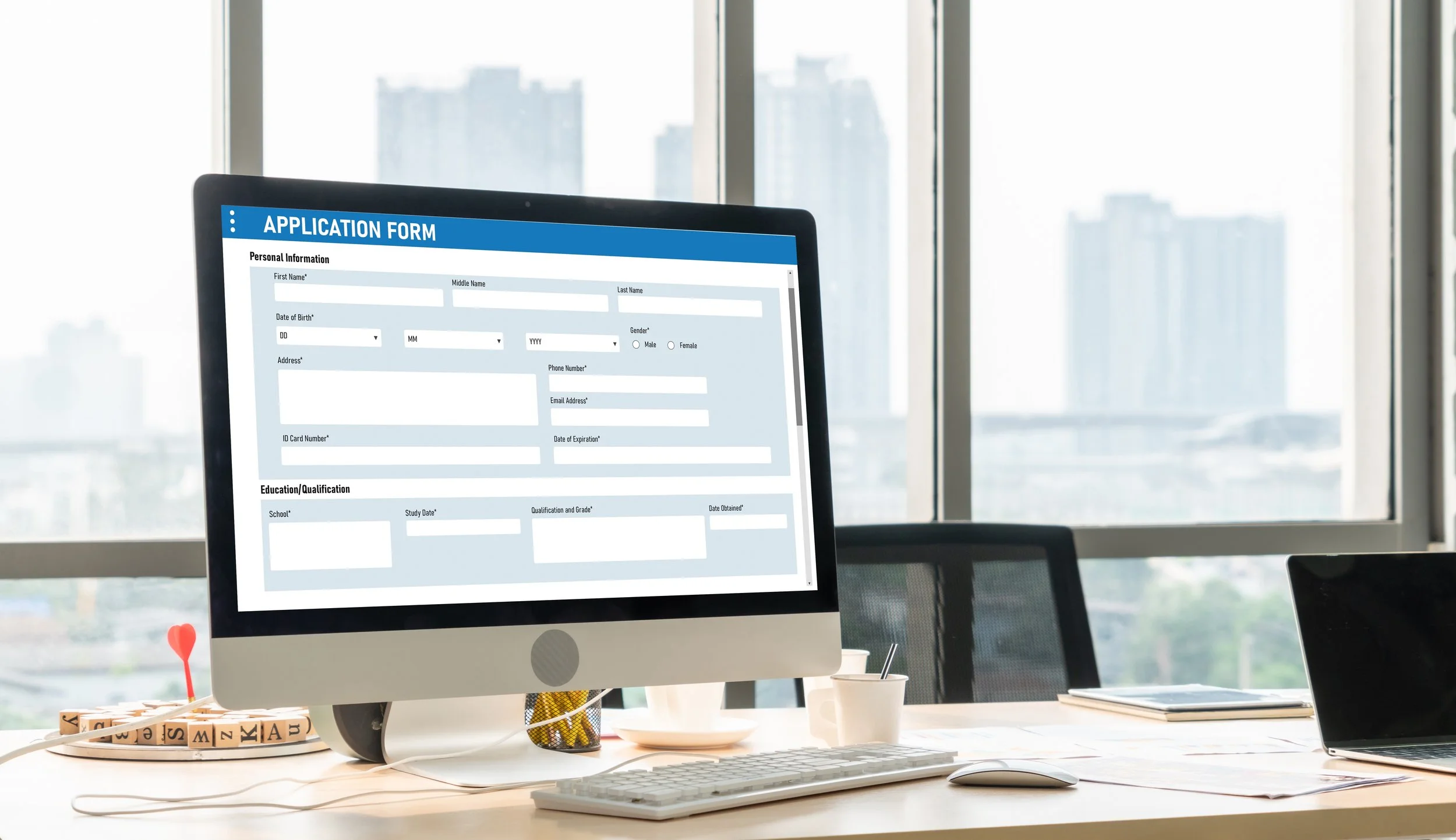 Computer monitor displaying an application form in an office with large windows showing city buildings in the background.