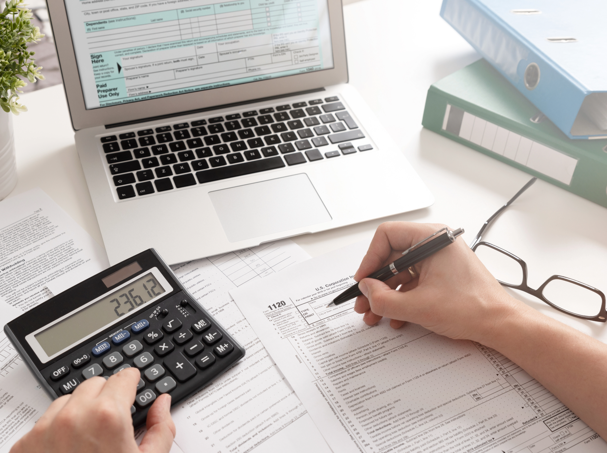 A workspace with a laptop displaying a tax form,a calculator and a pen over printed financial documents.