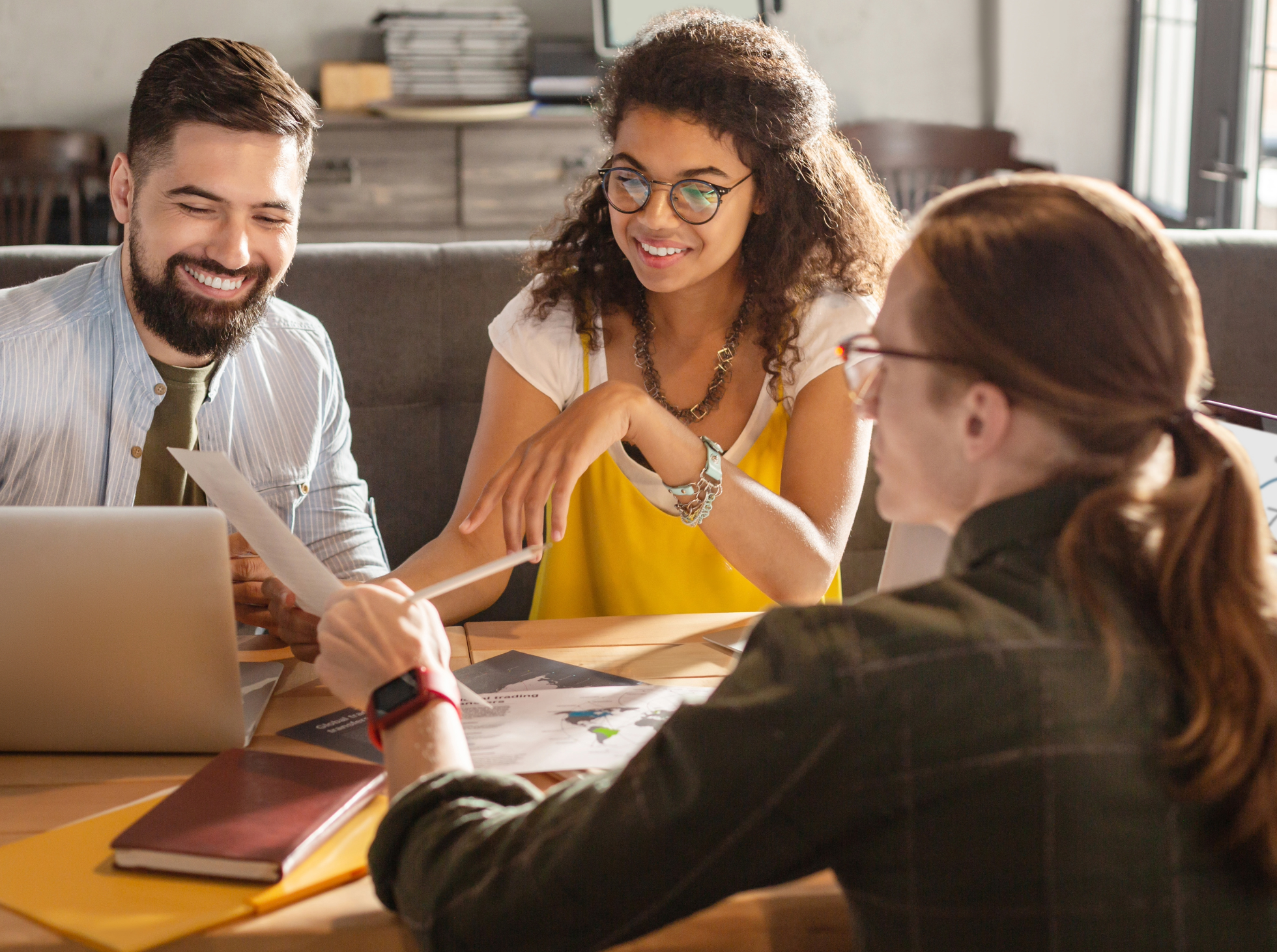 Three people engaged in a discussion sit around a table in a modern office space.