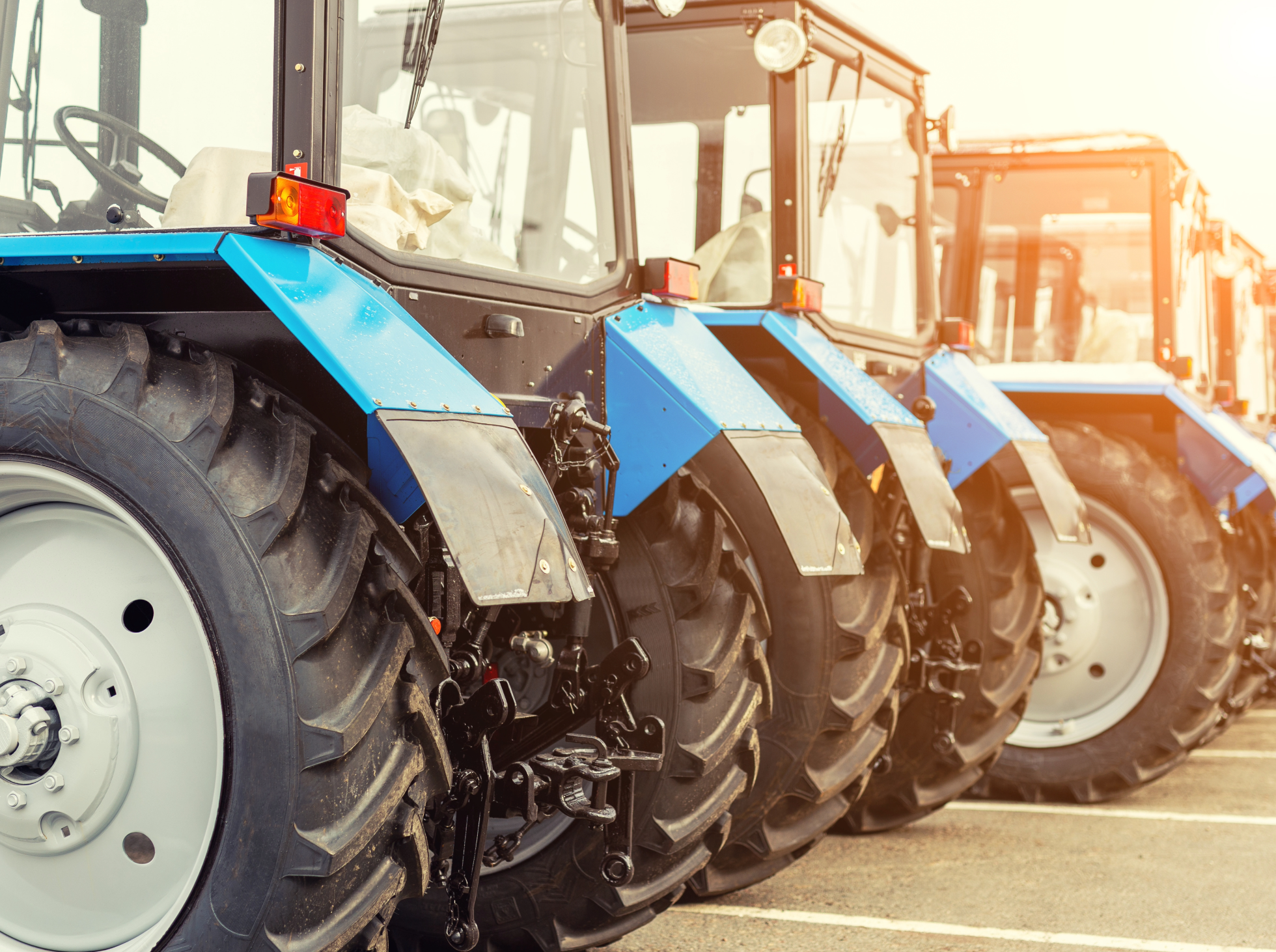 A row of tractors parked in a lot with their front wheels and tires visible.