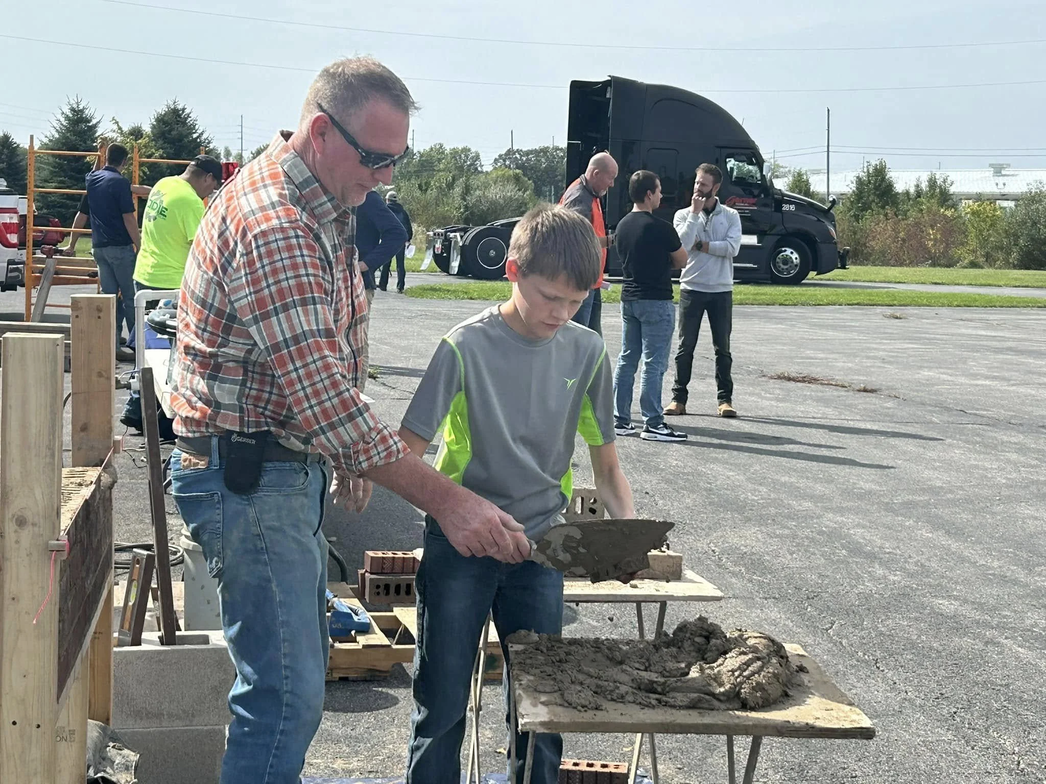 Man helping 8th grade boy with brick masonry at Raise the Bar's career connection day.
