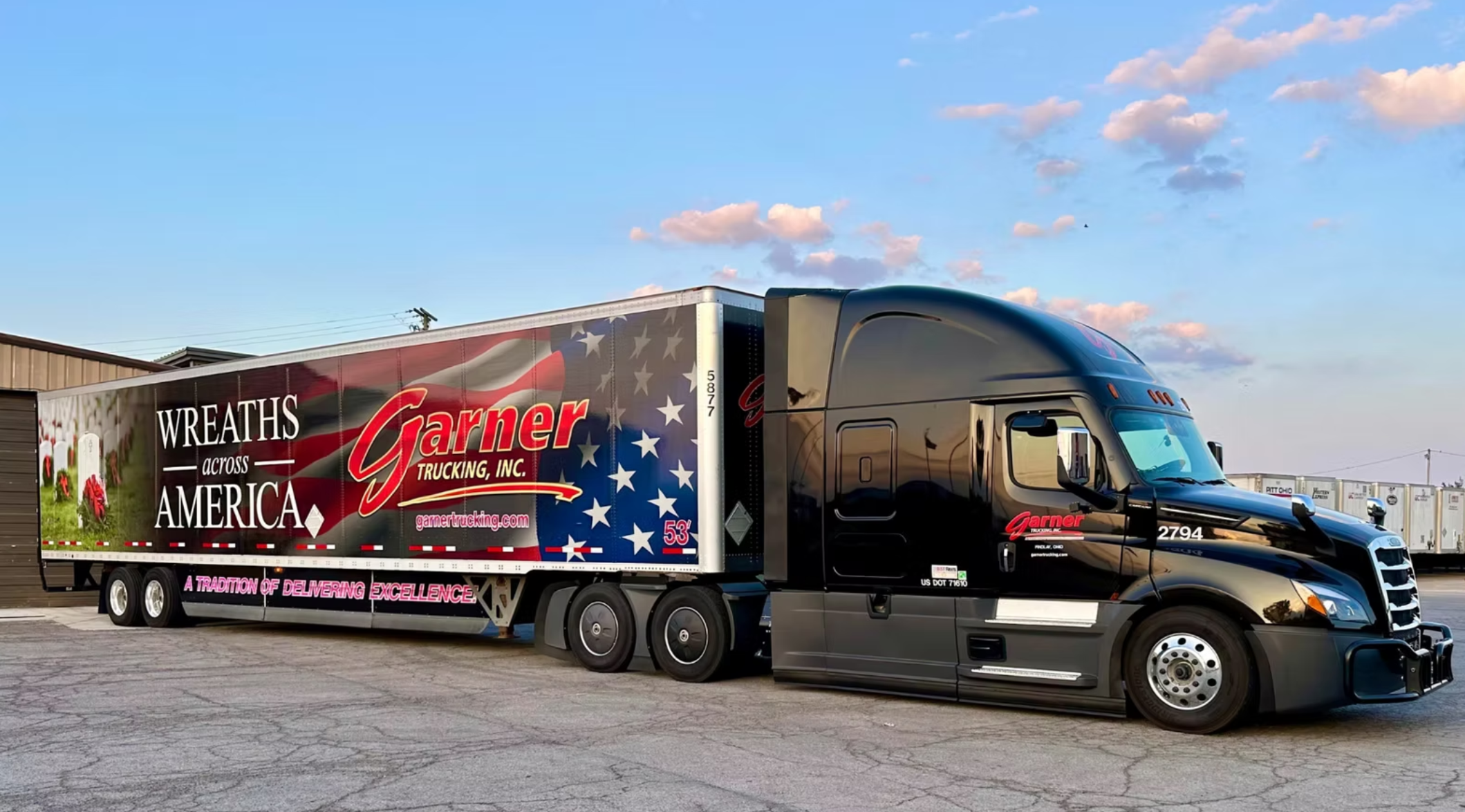 Black semi-truck with an American flag-themed trailer that reads "Wreaths Across America" and "Garner Trucking, Inc." parked in a lot.
