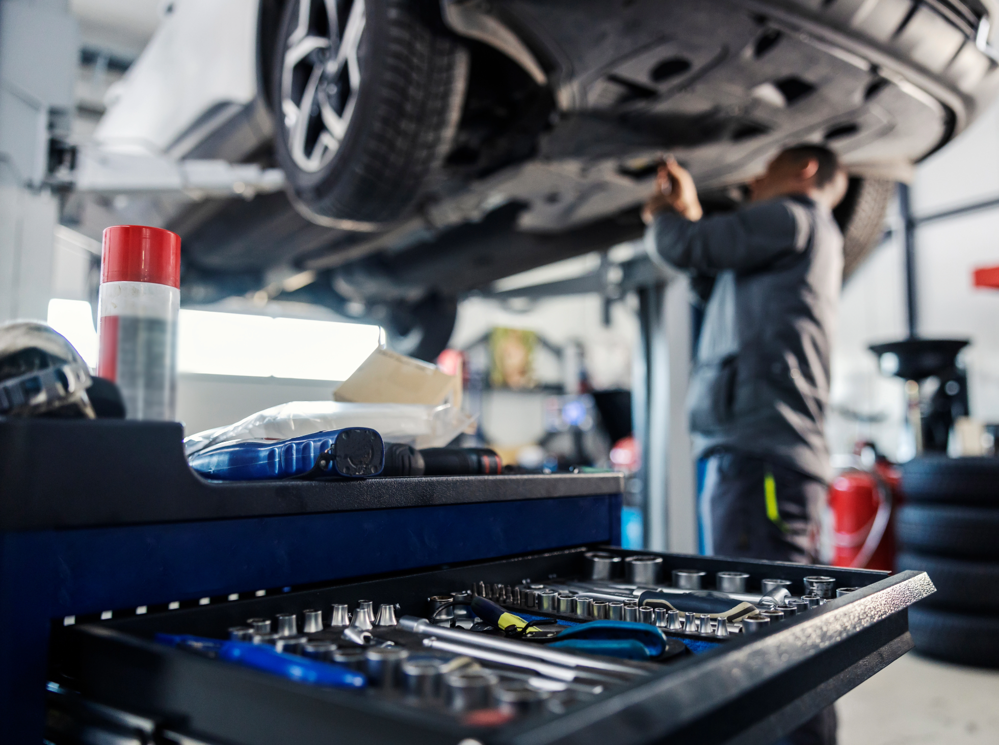 Mechanic working under a raised car in an auto repair shop.