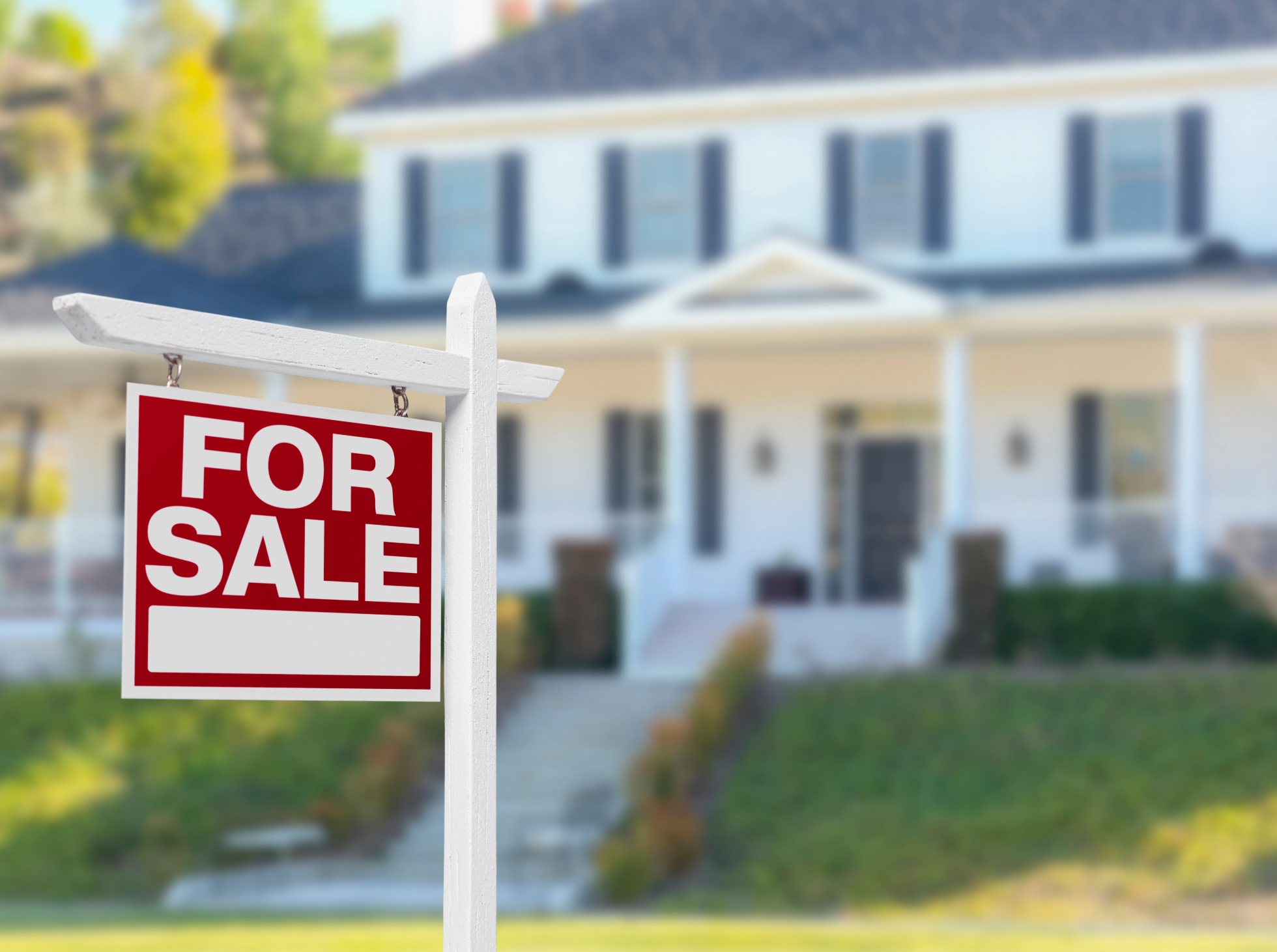 A 'For Sale' sign placed in front of a suburban house.