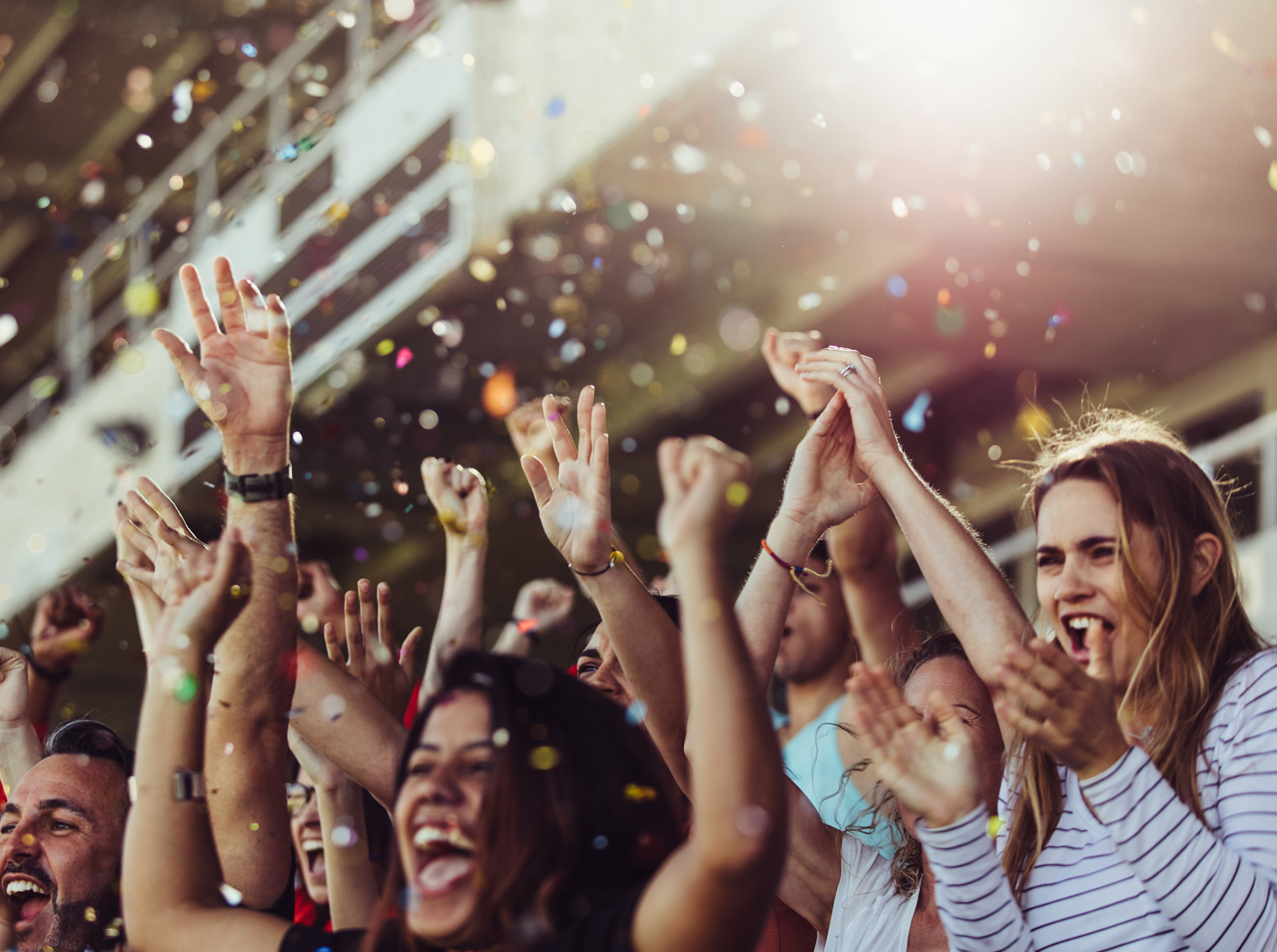 A crowd of people at a celebration with hands in the air and colorful confetti.