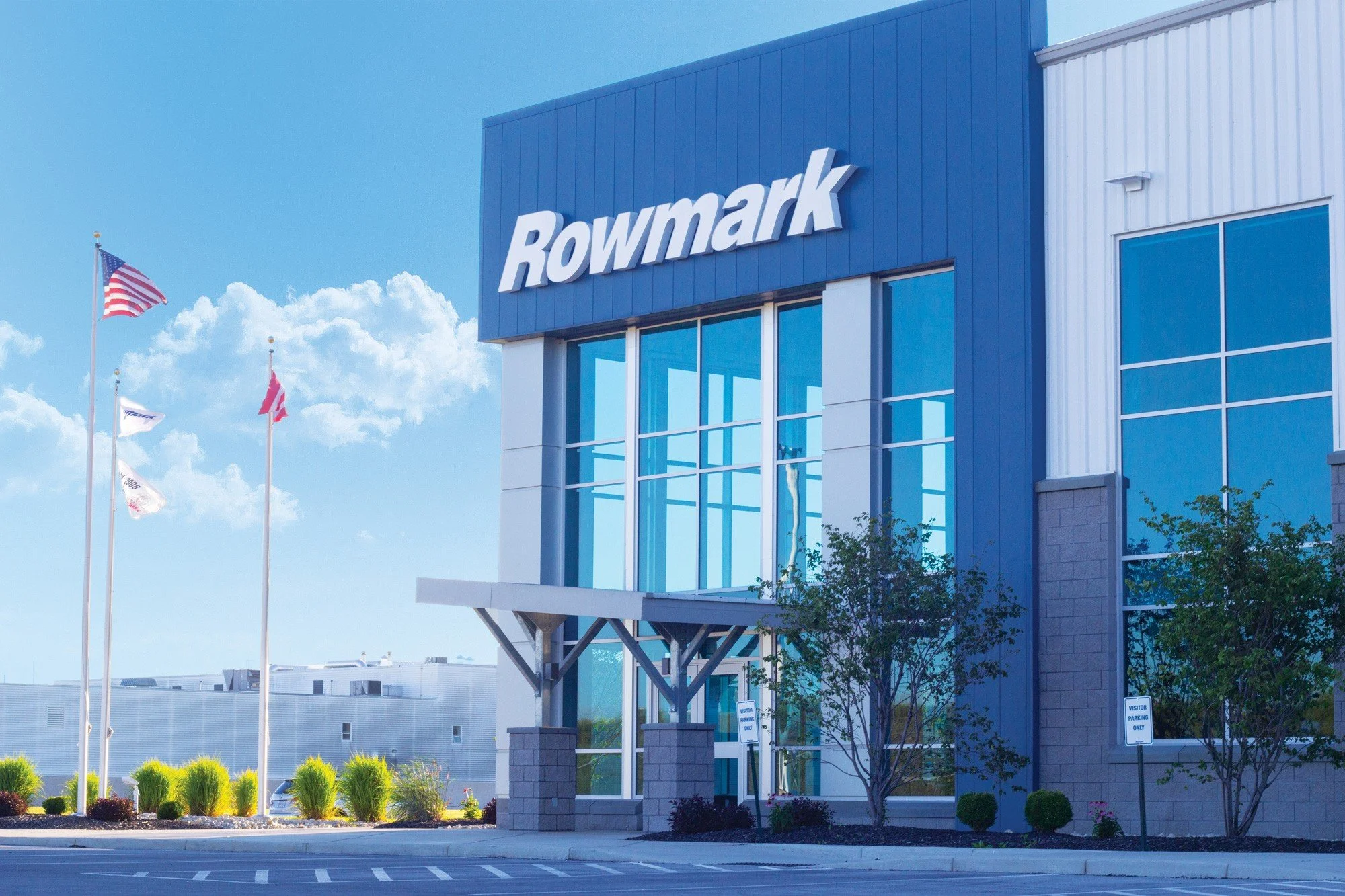 Exterior of the Rowmark building with blue facade, large windows, and flags.
