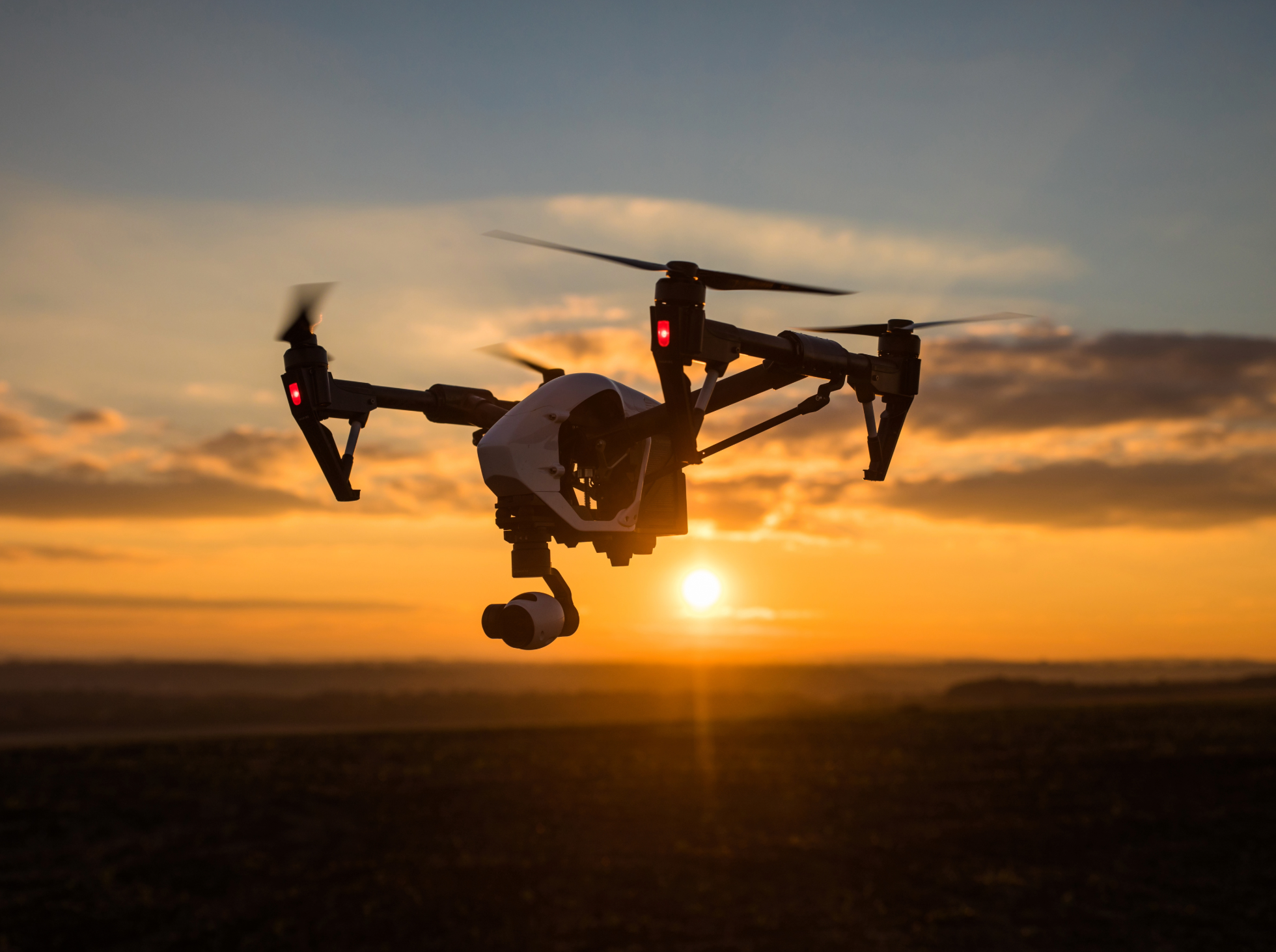 A drone flying at sunset with the sky filled with clouds and the sun near the horizon.