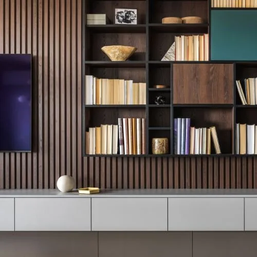 Wooden wall with built-in shelves filled with books, decorative objects, and framed photos, and a white cabinet below with a spherical sculpture and small gold item on top.