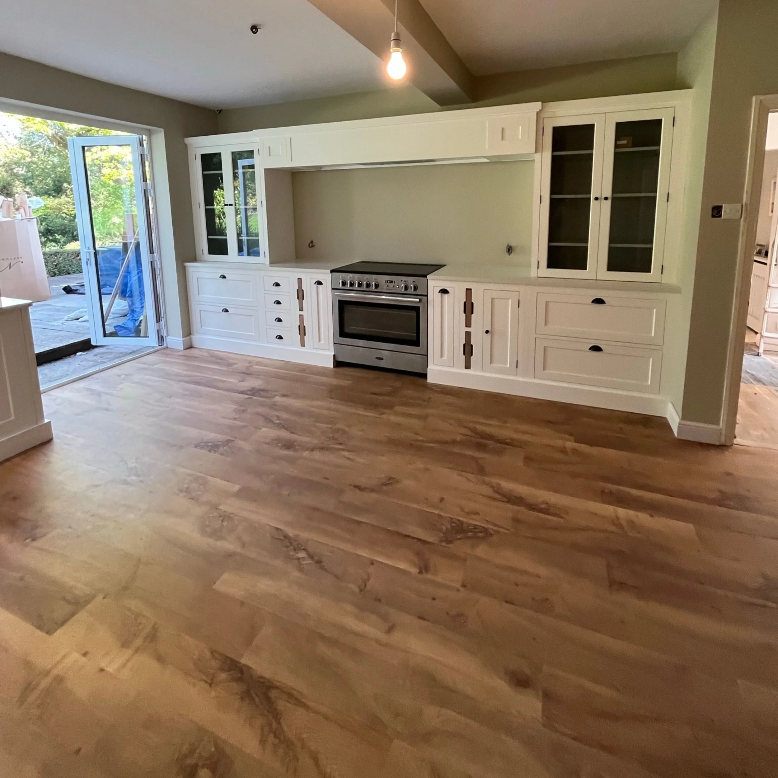 Empty kitchen with white cabinets, a stainless steel oven, and wooden floors.