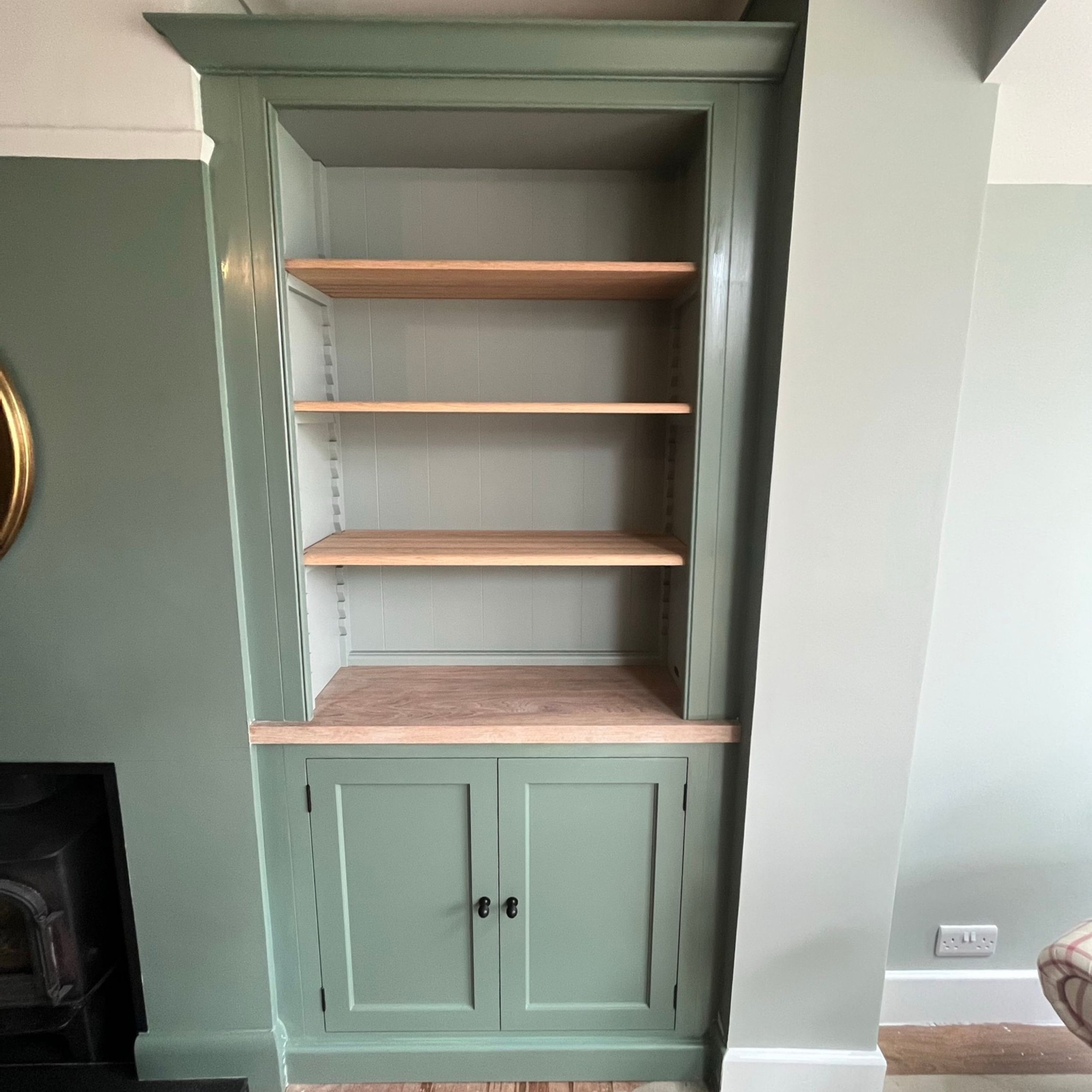 Empty built-in bookshelf with four wooden shelves and green cabinet doors at the bottom, in a room with light-colored walls.