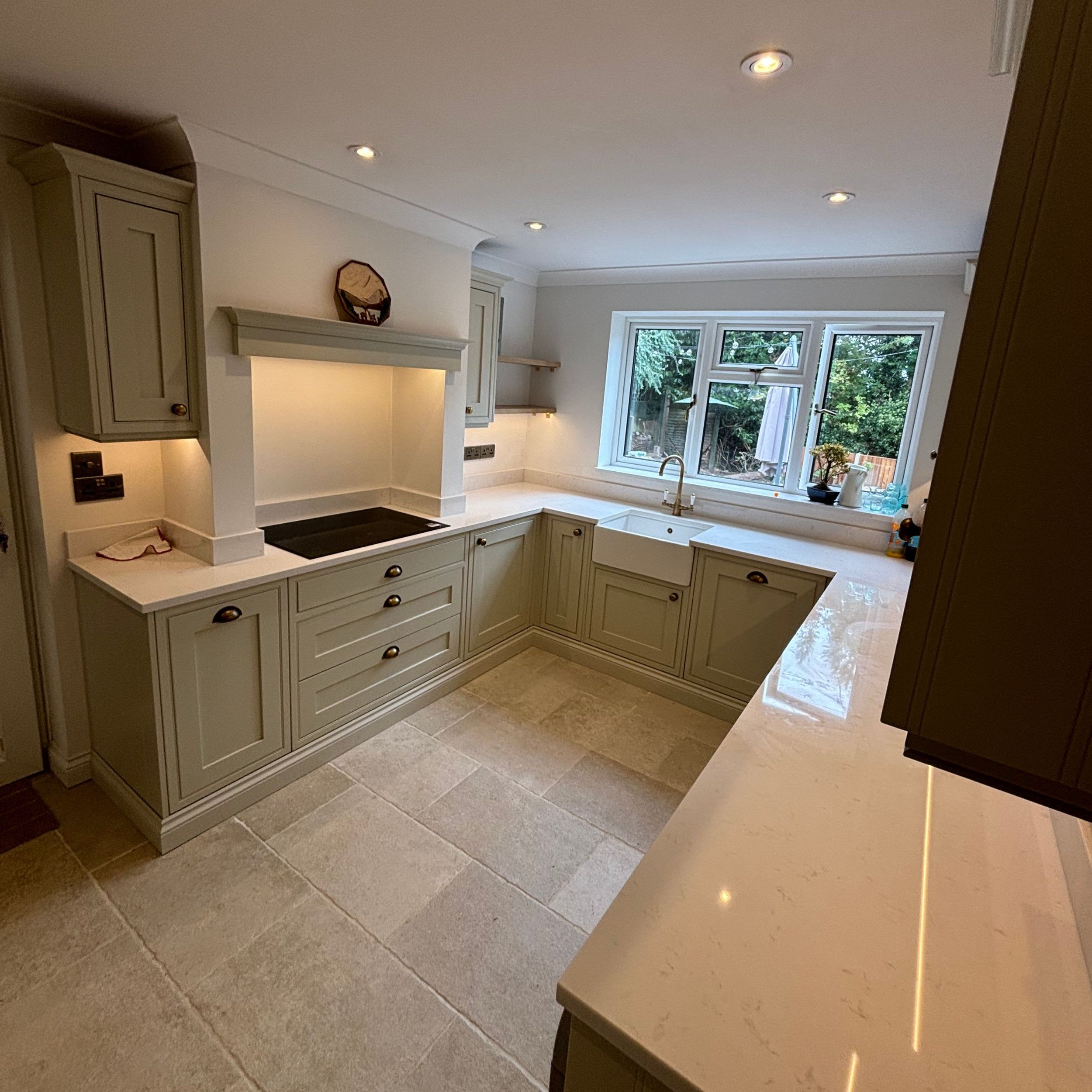 Bright kitchen with L-shaped beige cabinetry, white countertops, a large window, and a cream-colored tiled floor.